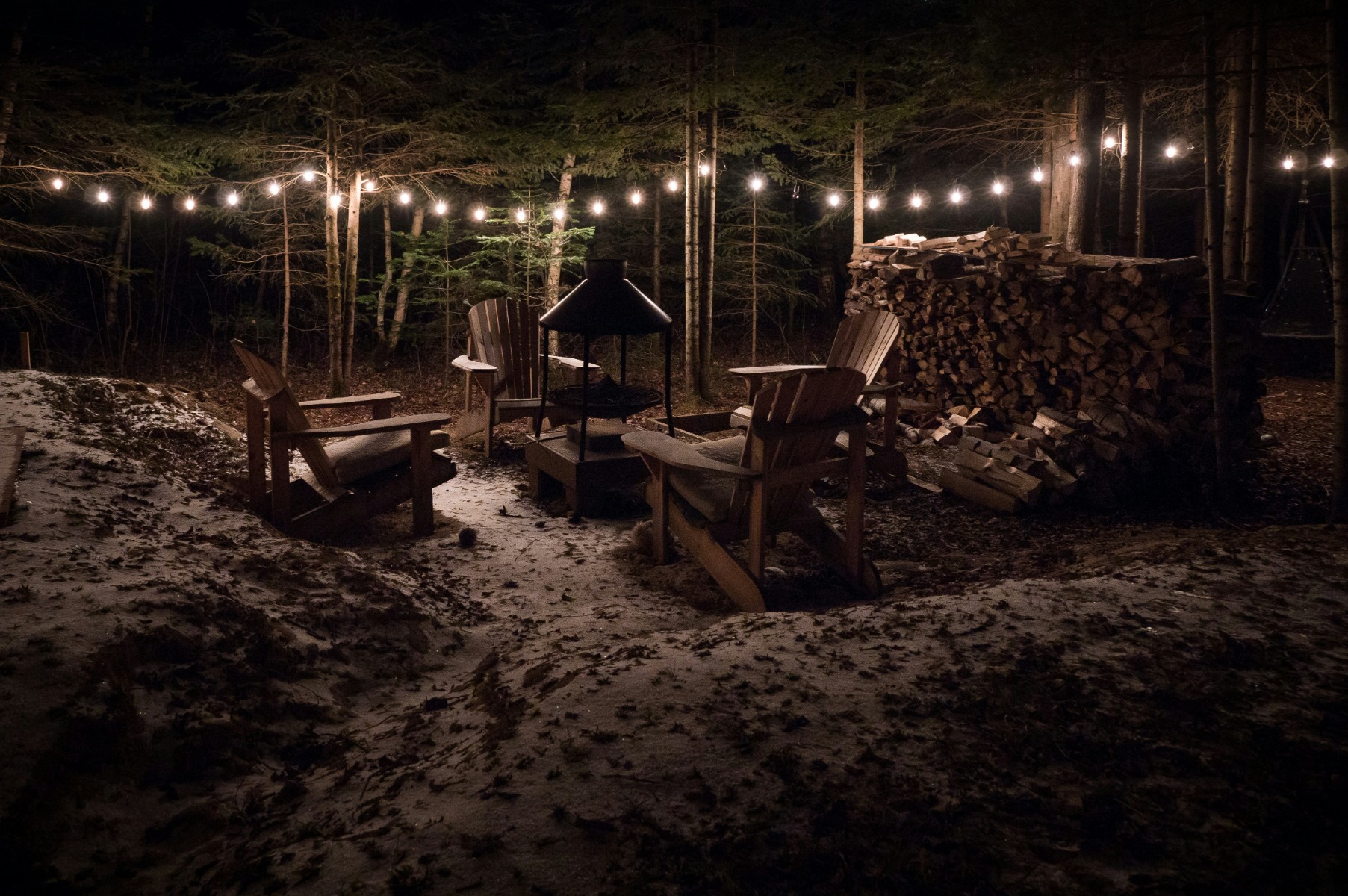 Fireplace in a garden surrounded by wooden chairs and pile of logs