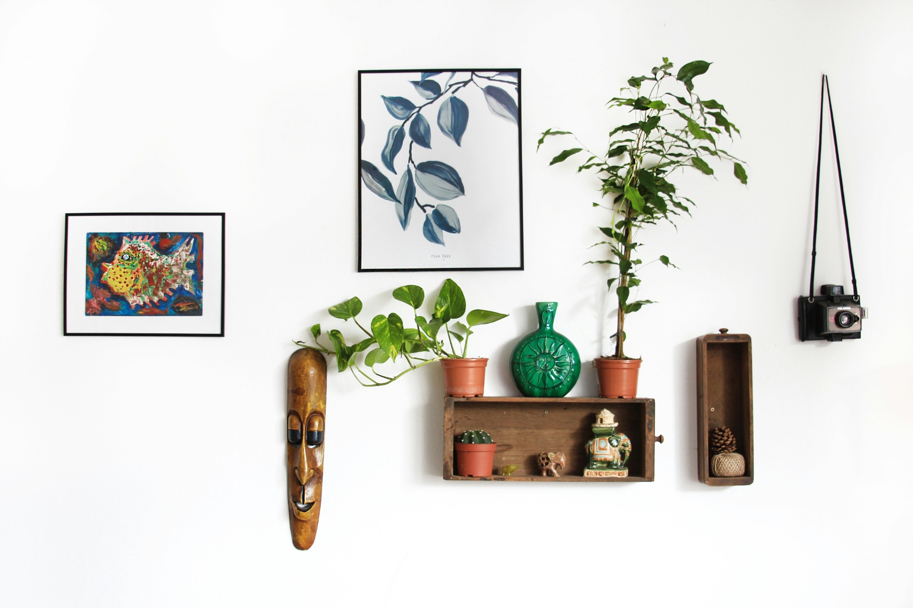 White wall with artwork, small plants and a wooden mask