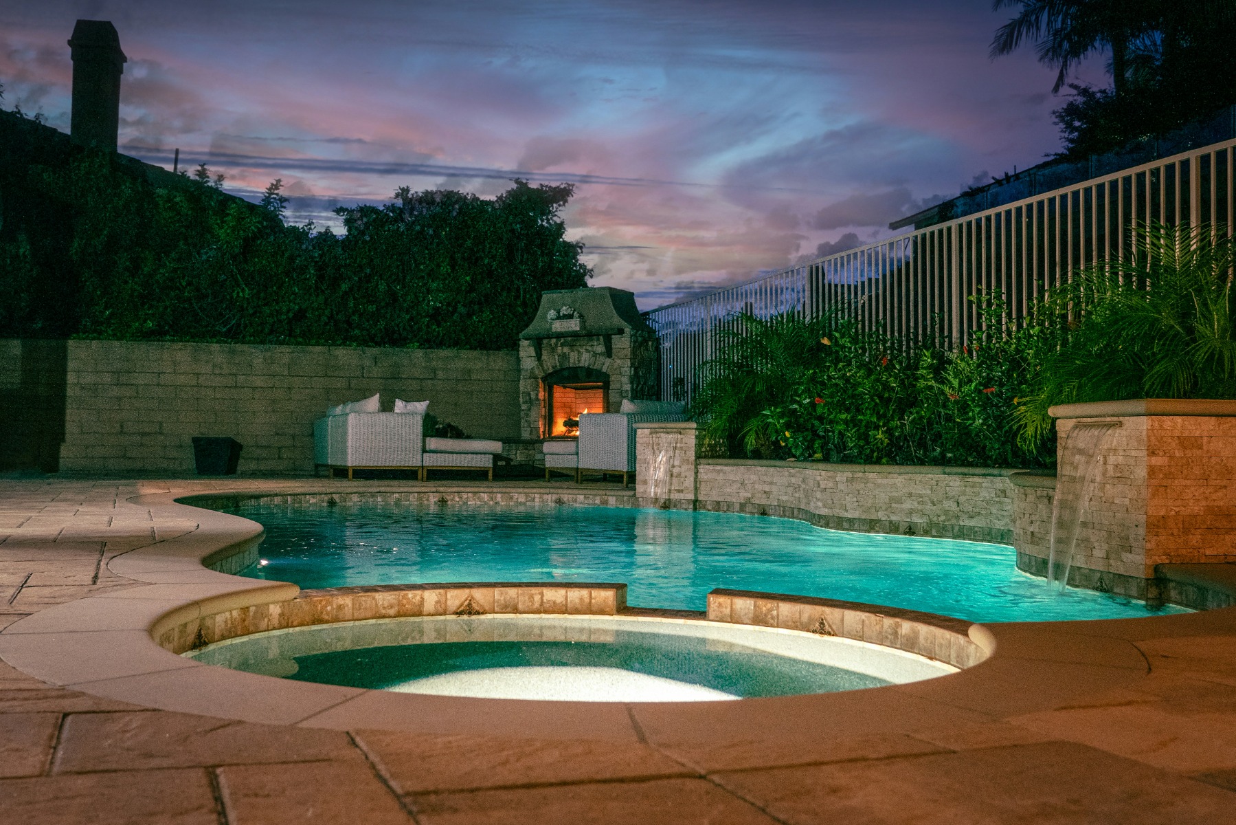 Outdoor pool with fireplace and sofas in the corner at nighttime